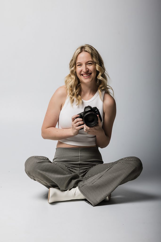 Photo of the owner of Dance Captures sitting down holding a camera and smiling